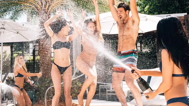 three people dance as someone sprays champagne on them