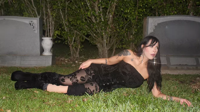 a woman in a black corset and black floral tights lays in the grass at a cemetry