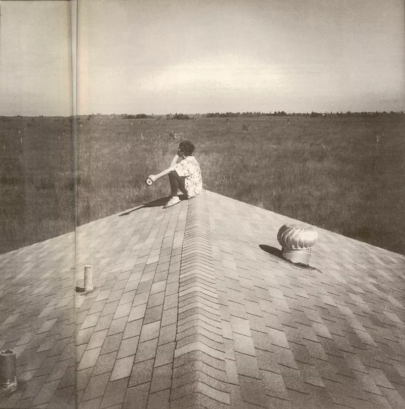 Image: reproduction of a black and white photo of a woman sitting on the roof of a house at the edge of the Florida everglades