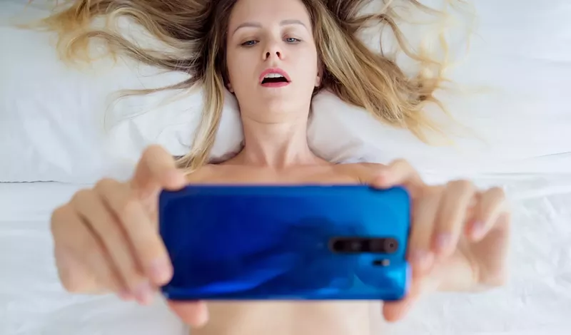 Image: Young sexy woman posing in front of smartphone in his hand and working as webcam model