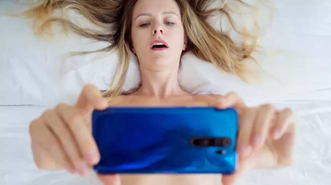 Young sexy woman posing in front of smartphone in his hand and working as webcam model