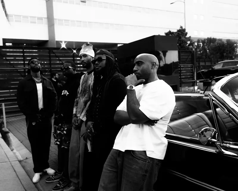 Image: group of men sitting by a car.