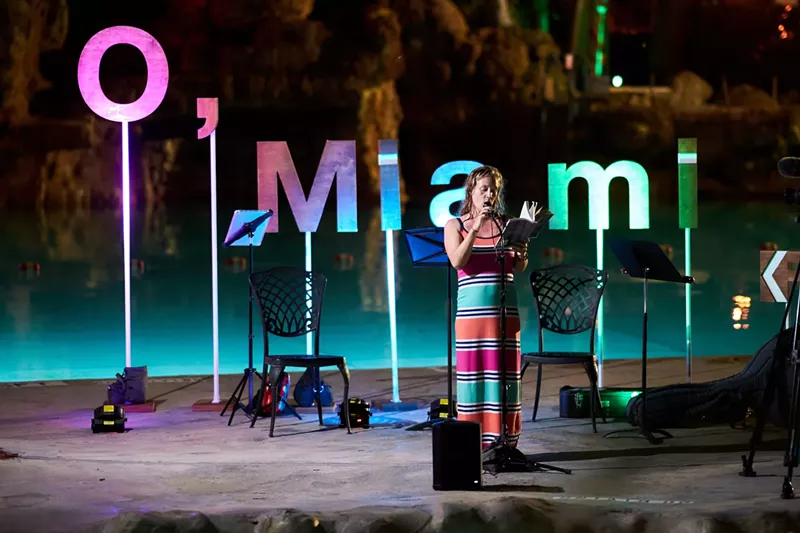 Image: a person reads a poem in front of a backdrop that reads, "O, Miami"