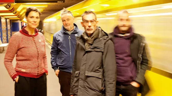 Picture of a four-piece band posing by a subway.