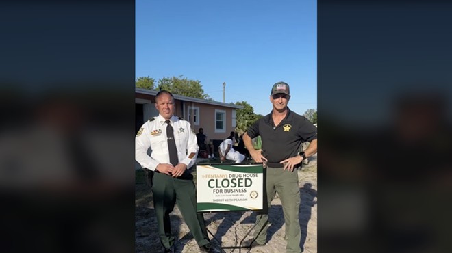St. Lucie County Sheriff Pearson stands in front of a house in front of a self-promoting sign that says "Fentanyl Drug House CLOSED for Business"