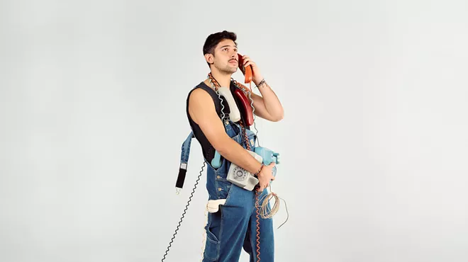 Portrait of a young man against a white backdrop holding many old telephones.