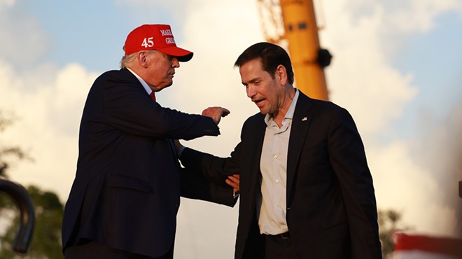 Donald Trump, wearing a red MAGA hat, grasps Marco Rubio by the arm and pats him on the shoulder onstage in Miami.