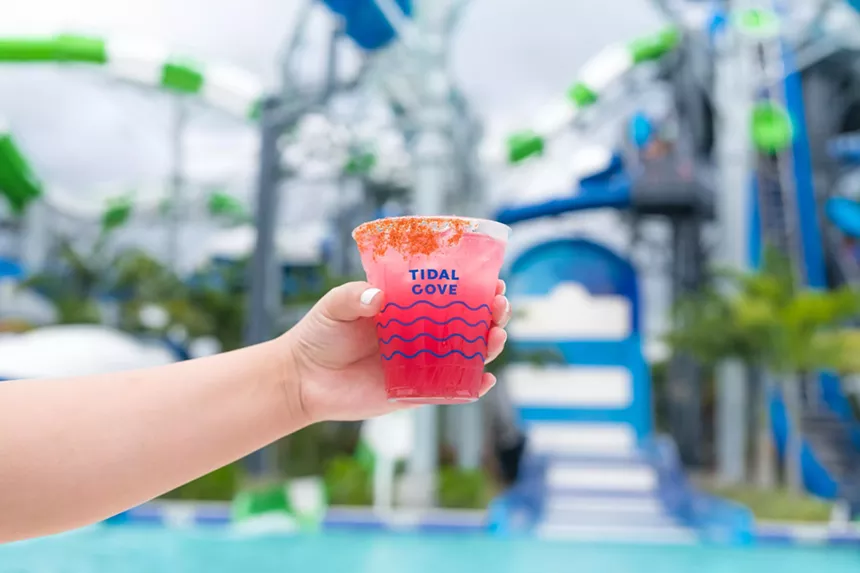 At JW Marriott Miami Turnberry Resort & Spa, a woman holds a cocktail in front of the bottom of a water slide.