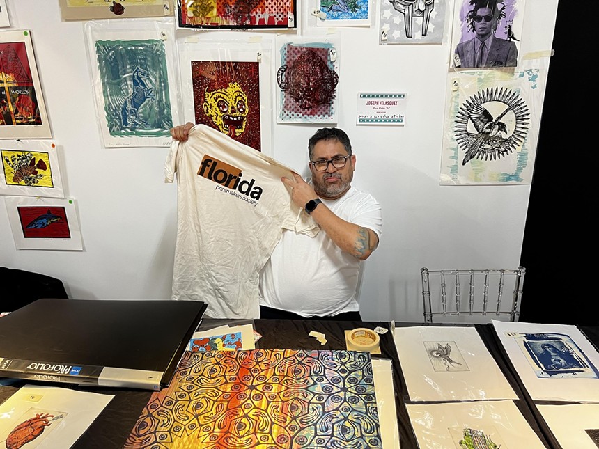 Artist Joseph Velasquez holds up a Florida Printmaking Society t-shirt