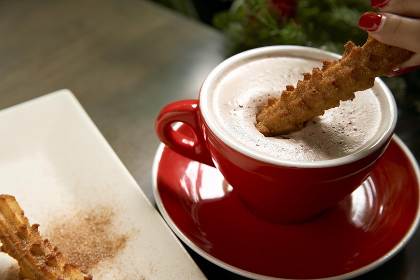 A churro being dipped in hot chocolate