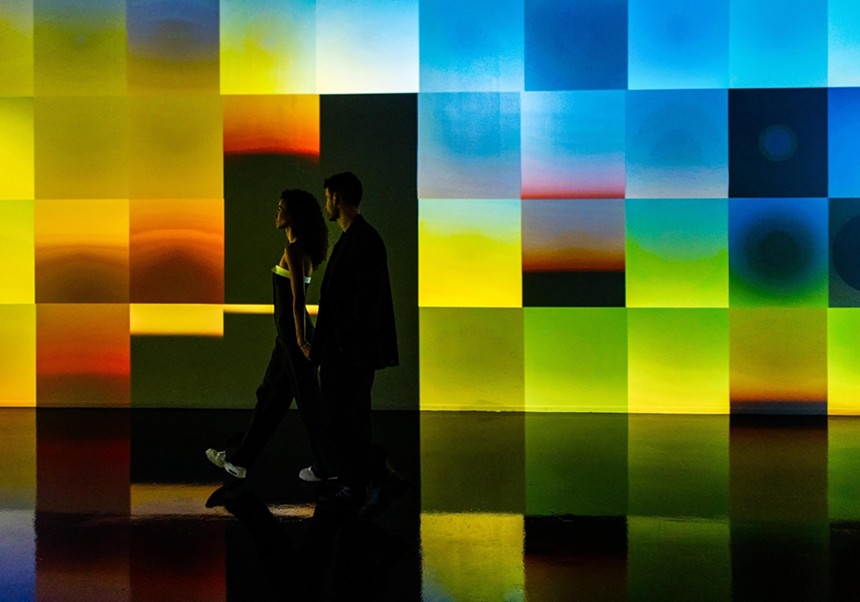 A couple holds hands while walking in front of an interactive art installation