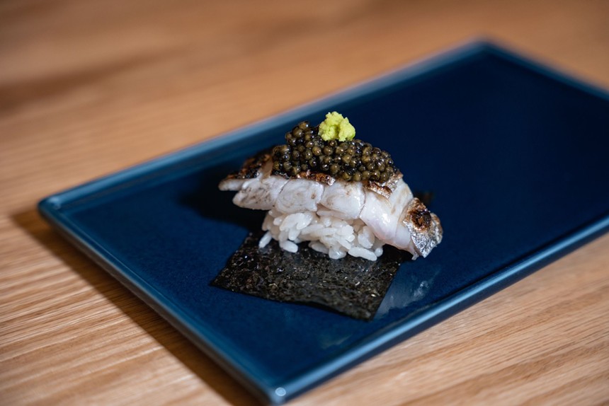 A delectable piece of squid nigiri topped with black caviar sits on a blue plate at Ogawa.