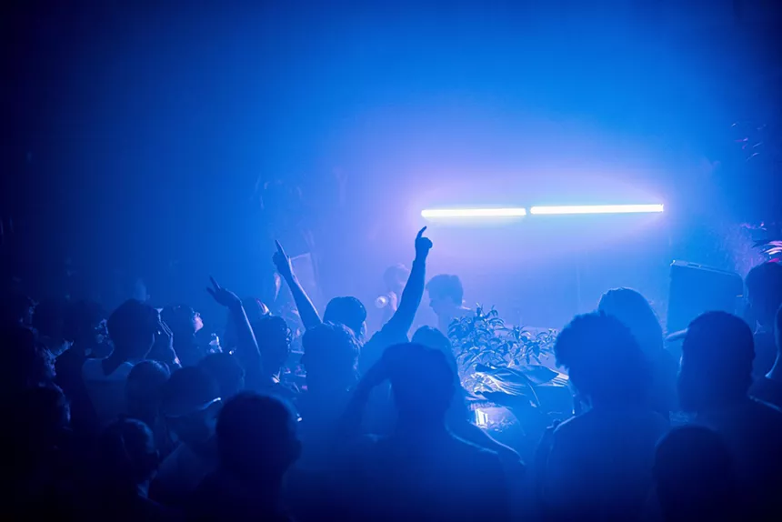 Partygoers awash in a blue light as Coffintext DJs behind the decks