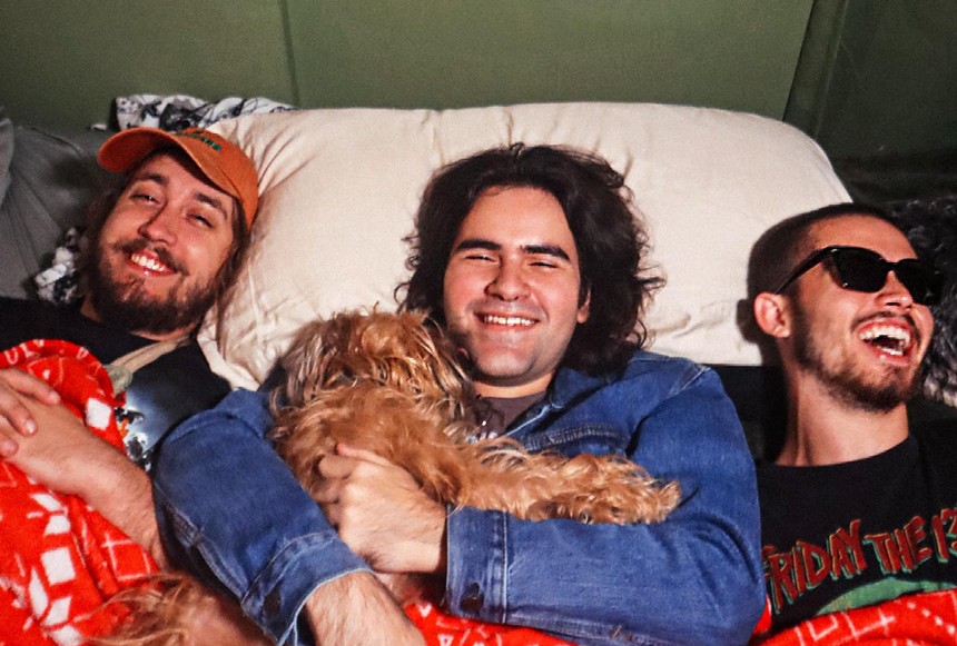 The three members of the Creature Cage in bed with a dog