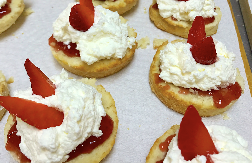 Biritsh scones covered in jam, cream, and a strawberry