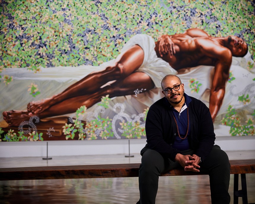 Aurin Squire sitting on a bench in front of Kehinde Wiley's painting of a sleeping man