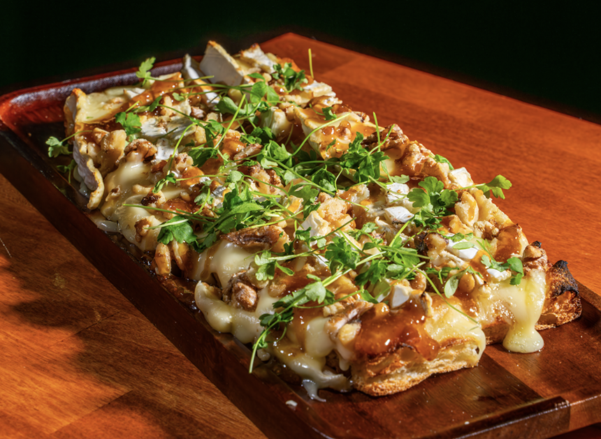 A cheesy flatbread on a wooden platter.