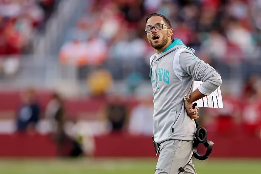 Miami Dolphins coach Mike McDaniel on the field, staring upwards while holding his headphones