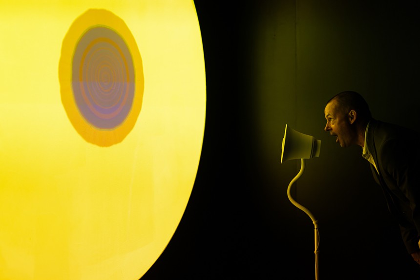 A man speaks into a microphone as the projection reacts to his voice