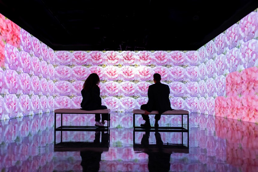 Two people sit on benches as projections take over the surrounding walls