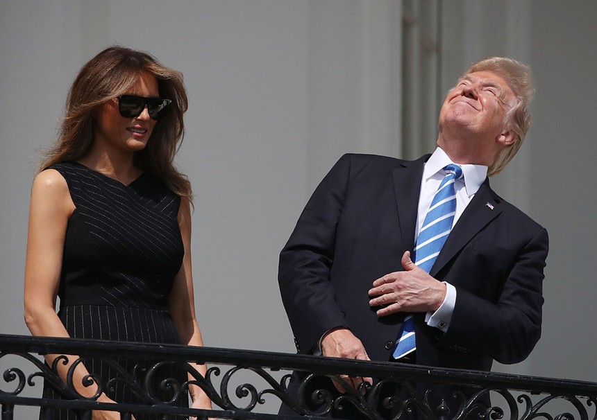 Color photo of U.S. President Donald Trump, wearing no eye protection, looking skyward from the Truman Balcony at the White House during the total solar eclipse of August 21, 2017, while First Lady Melania Trump, whose face is partially obscured by large, dark glasses, does not look up or, for that matter, at the camera.