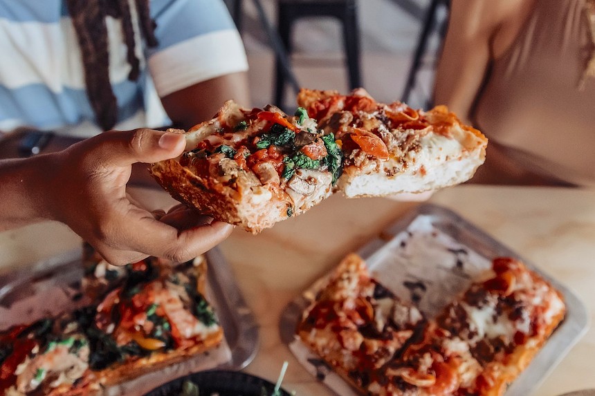 A hand holding a square slice of pizza