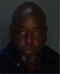 Booking photo of a murder suspect with a shaved head, heavy-looking eyelids and a goatee