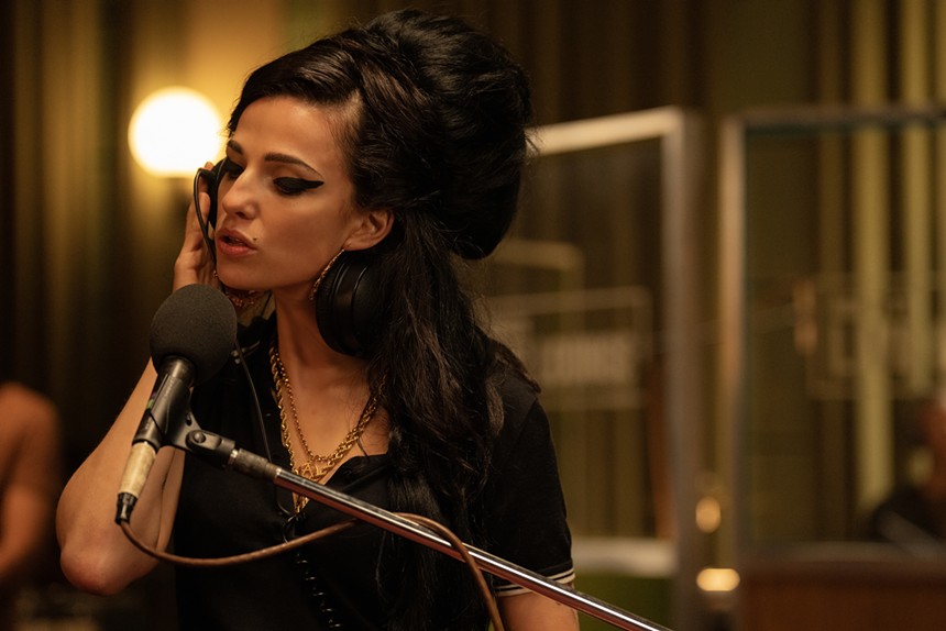 Marisa Abela portraying Amy Winehouse singing into a microphone