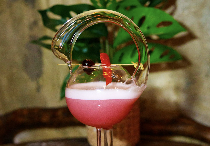 A pink cocktail in a funky glass with garnishes