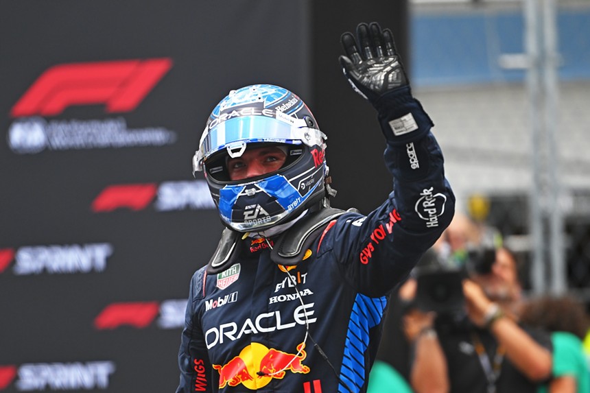 Max Verstappen in his race suit and helmet waves at the crowd