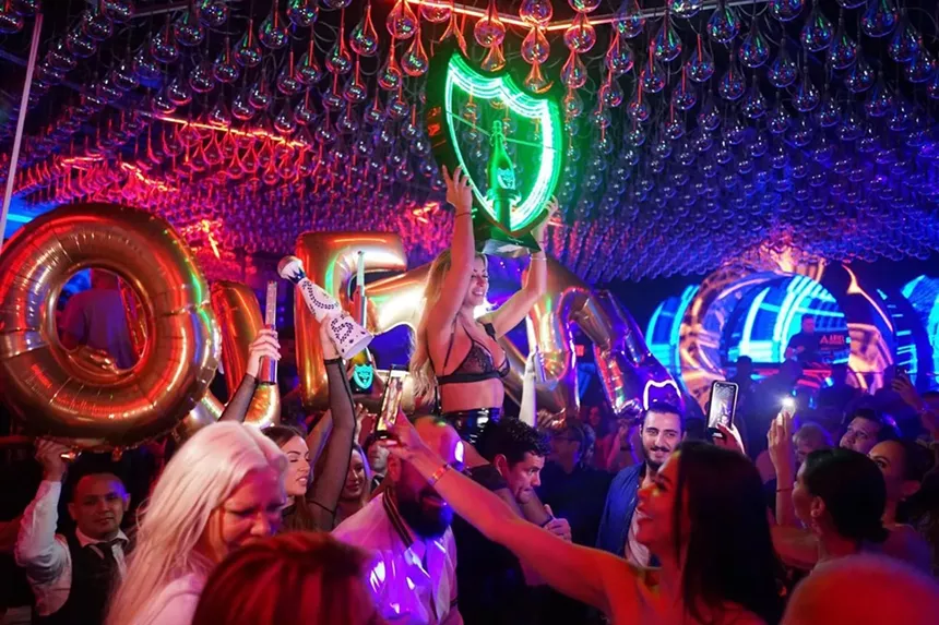 A woman hoisting up a bottle inside of Mynt Lounge