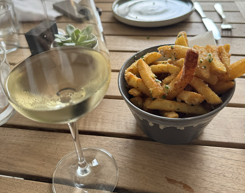 White wine on a wooden table with a bowl of seasoned French fries