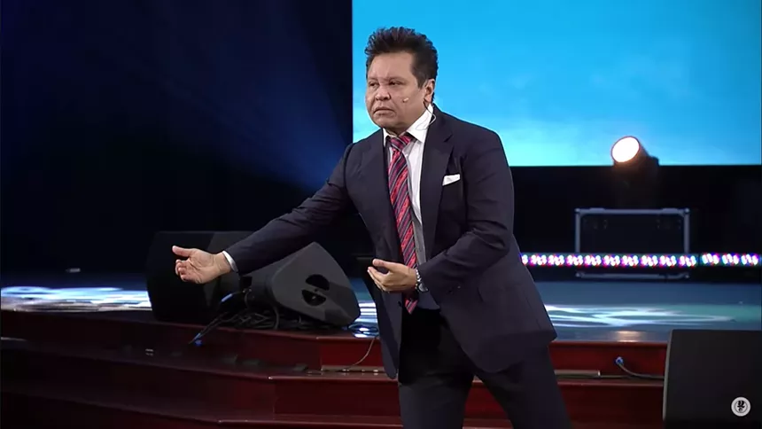 Preacher Guillermo Malonado extends his to the side of his body while giving a sermon to a huge crowd