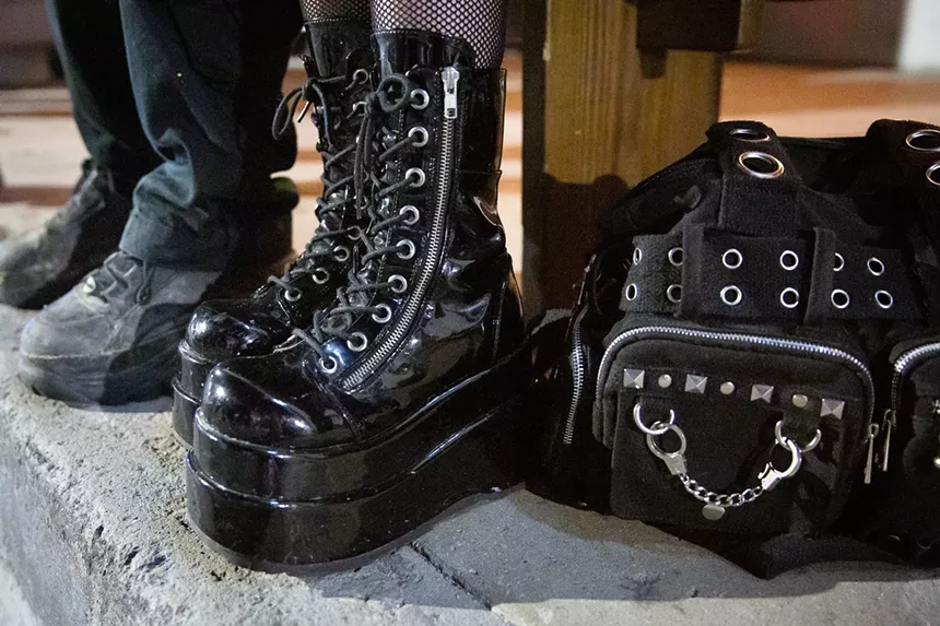 A black backpack with silver studs next to someone's black platform boots