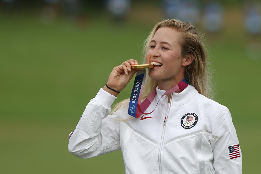 Golfer Nelly Korda puts an Olympic gold medal under her front teeth