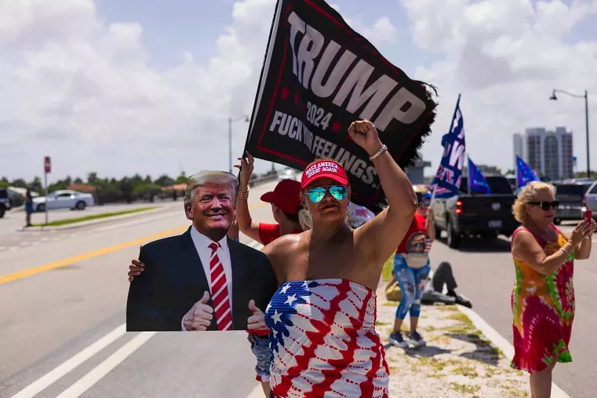 A woman in an American flag dress holds up a cutout picture of Donald Trump outside Mar-a-Lago