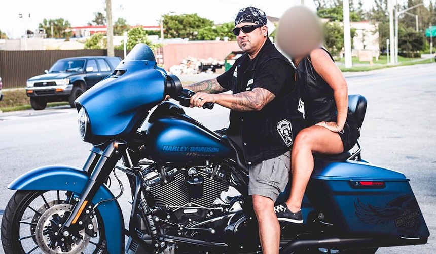 Danny Torress posing on his blue Harley Davidson motorcycle.