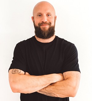 bearded, bald man standing with arms crossed