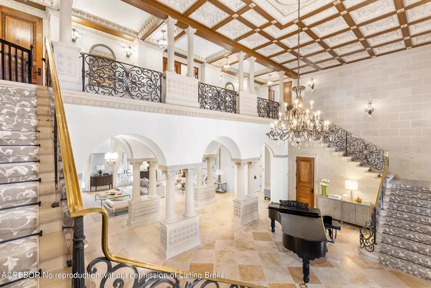 Grand entrance with a sweeping staircase, chandelier, ornate ironwork, and a grand piano