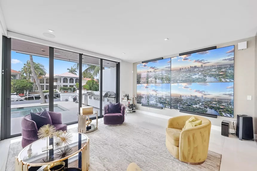 A living room with four flatscreen TVs pushed together and three chairs