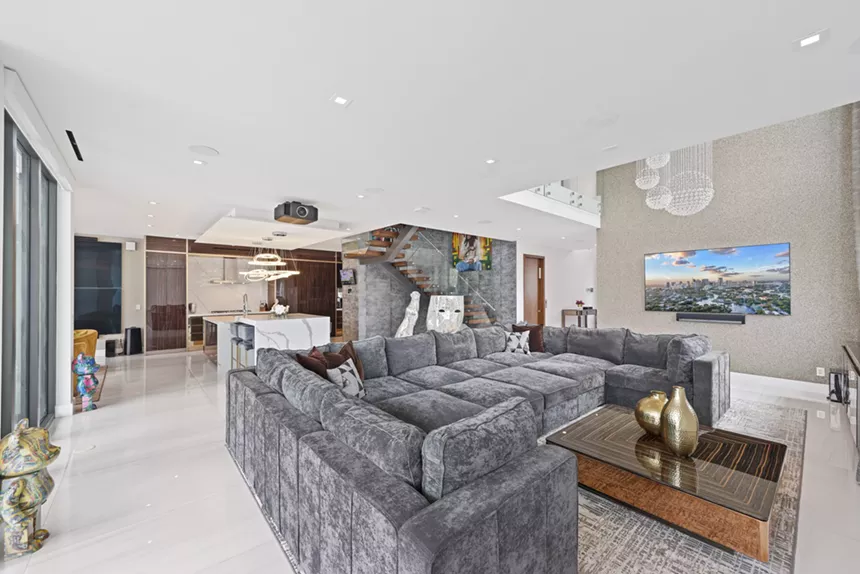 A large living room inside Mike Pouncey's mansion. A large grey couch sits next to the kitchen.