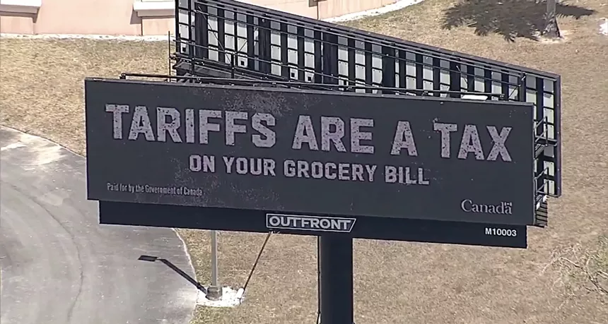 screenshot of an aerial shot of a billboard that reads: "TARIFFS ARE A TAX ON YOUR GROCERY BILL."