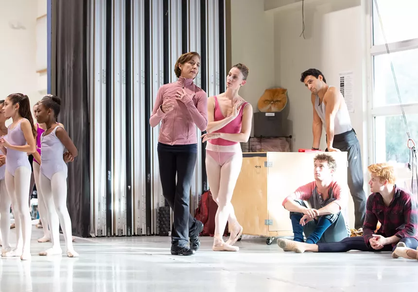 a dance instructor models a pose for a ballet dancer as other dancers look on