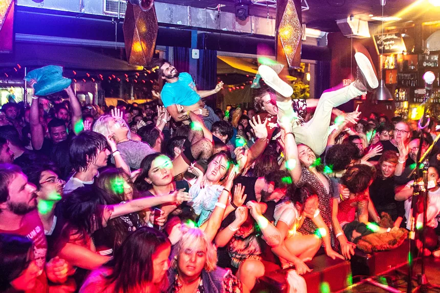 people crowdsurf over a crowded audience in front of a stage