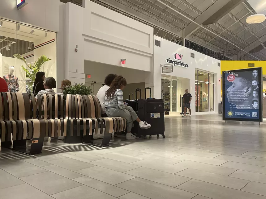 Two people sit alongside a pair of suitcases in a mall