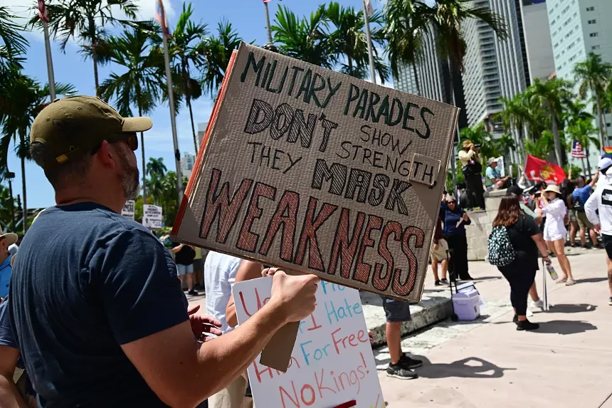 protester holds up homemade sign reading "Military parades don't show strength, they mask weakness"