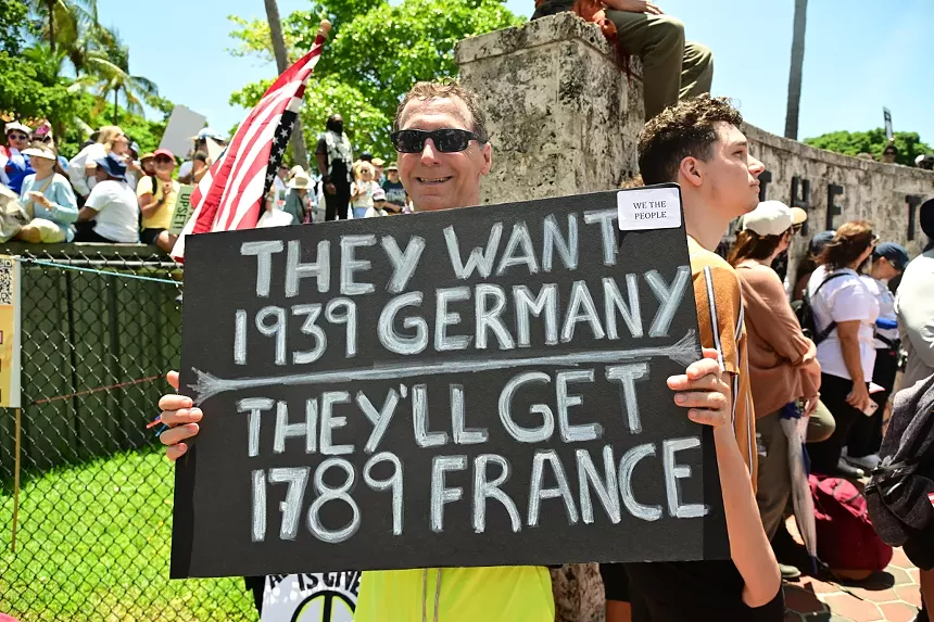 A protester holds a sign reading, "They want 1939 Germany/They'll get 1789 France."