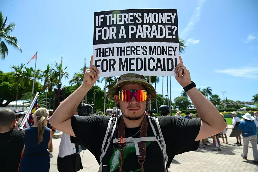 A man holds a sign reading, "if there's money for a parade, then there's money for Medicaid"