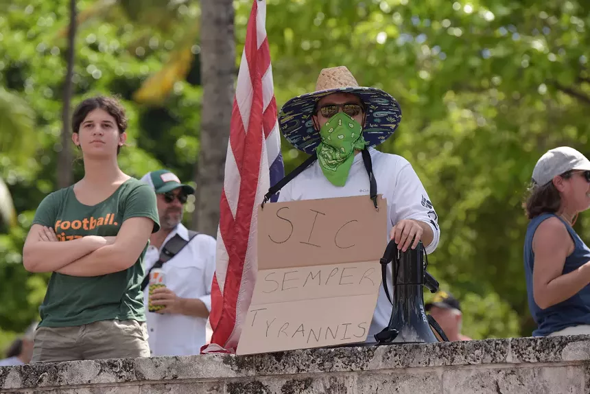 A demonstrator holds a sign saying "sic semper tyrannis," a Latin phrase translating to "thus always to tyrants