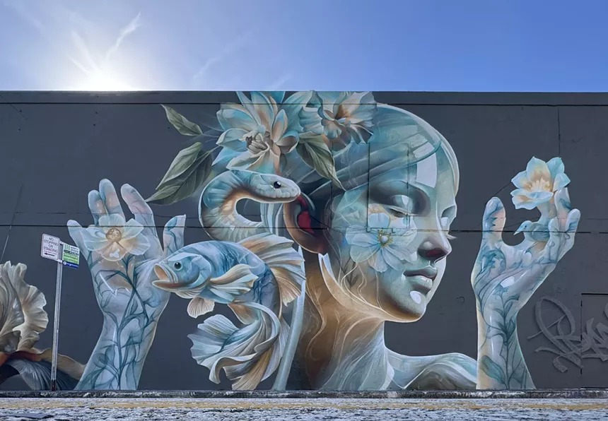 a mural on a black wall shows a translucent female figure holding flowers in her hands, surrounded by a fish, snake, and flowers